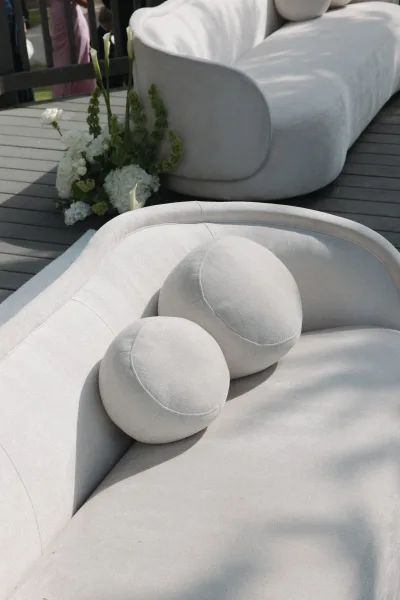 Wedding lounge seating arranged as an outdoor reception lounge with a curved sofa on a wood deck overlooking a lush garden lawn.