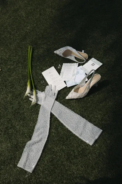 Wedding details flat lay with bridal accessories styling, highlighting beaded gloves on a grass lawn.
