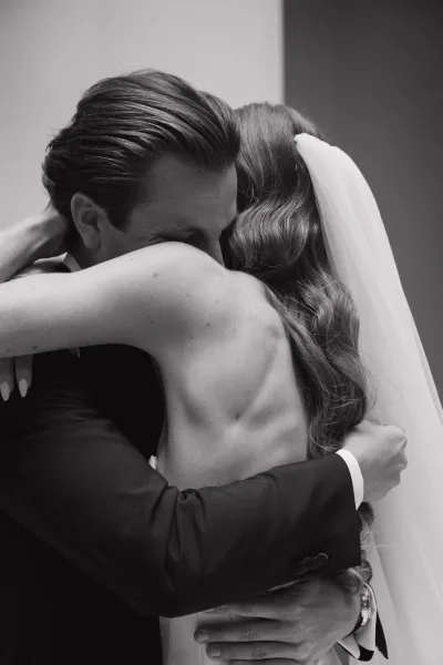 Wedding hug in a candid wedding moment as the groom holds the bride with veil, a timeless black and white portrait capturing their quiet emotion.