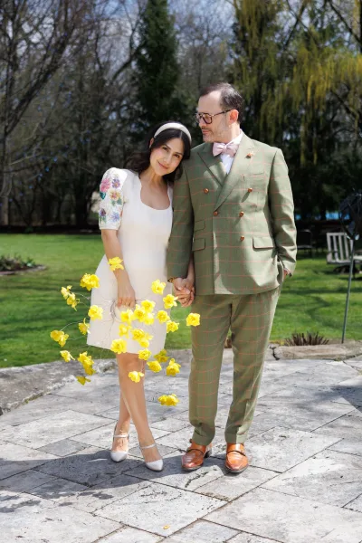 Couple portrait of a bride and groom holding hands, her yellow flower bouquet bright against his suit as they stand together on a stone patio.
