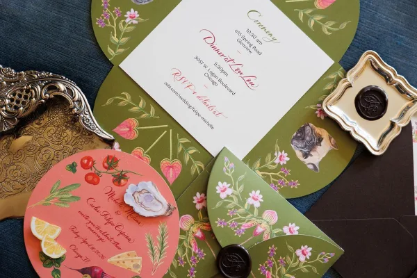 Wedding invitation suite featuring floral wedding invitations with wax seals arranged on blue fabric.
