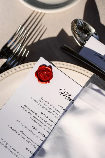 Wedding menu with wax seal stationery rests on a linen tablecloth, featuring minimal black and white design and refined serif typography.