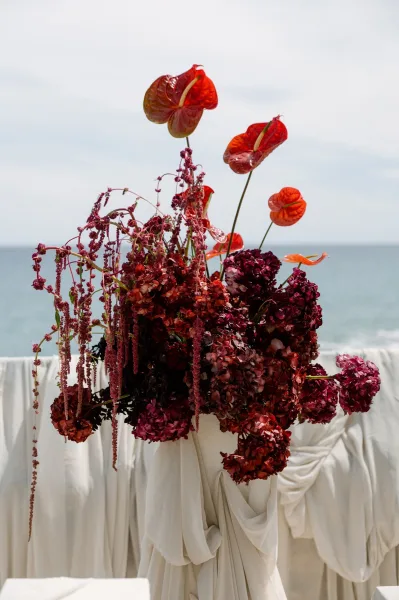 Wedding floral arrangement featuring red anthurium wedding flowers, sculptural and oversized, styled before an open ocean and sky horizon.