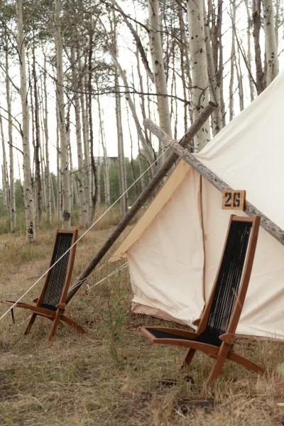 Glamping tent setup with a canvas bell tent, guy lines, and wooden lounge chairs, marked by a tent number sign in an aspen forest