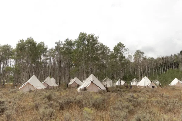 Glamping wedding tents arranged as a bell tent wedding village, with canvas tents and guy lines set in an aspen meadow under cloudy sky