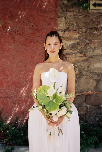 Bridal portrait of a bride holding bouquet against a red stucco wall, captured in natural light with a modern, minimalist wedding style.