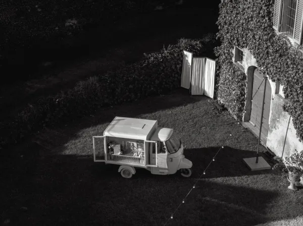 Mobile bar cart serving as a chic cocktail hour idea, trimmed with string lights, set against an ivy-covered wall on a grass lawn.
