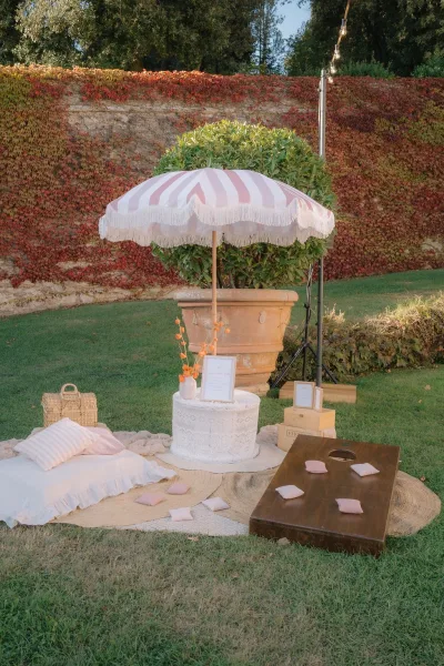 Cocktail hour lounge at a garden cocktail hour, styled with a striped fringe parasol beside an ivy-covered stone wall on a grass lawn.